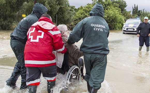 personas de la cruz roja y guardia civil ayudando a un hombre en silla de ruedas a moverse en una calle inundada