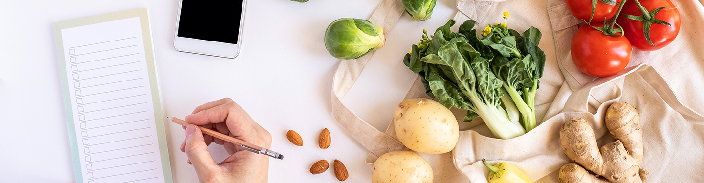 Persona haciendo una lista de la compra con alimentos a su lado