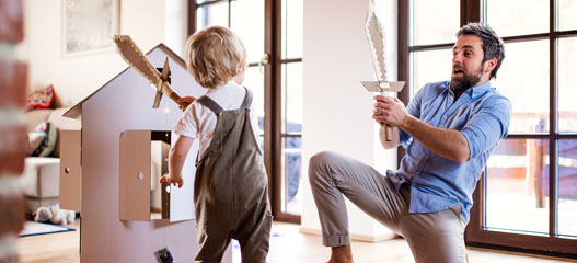 padre jugando con hijo con espadas de cartón en casa