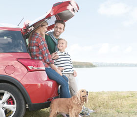 Familia contenta apoyada en el maletero de un coche con su perro y el mar de fondo